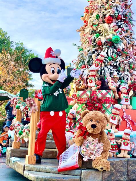 mickey mouse standing in front of a christmas tree and teddy bear on the steps outside