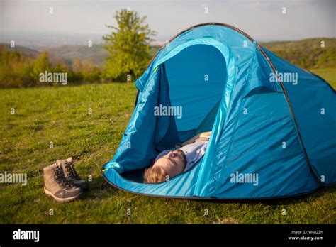 one young man, sleeping in small tent, in a grass field, in mountain ...