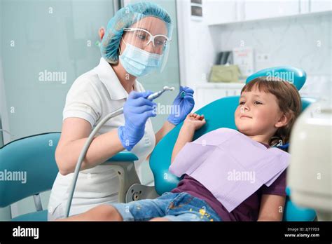 Dentist looking at frightened female child before teeth-polishing ...