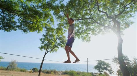 Athlete walking in slackline in the park with sea and blue sky on ...