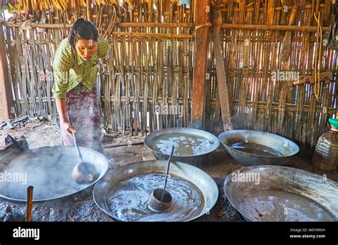 BAGAN, MYANMAR - FEBRUARY 26, 2018: Burmese farmer is stirring palm sap in large metal boilers ...