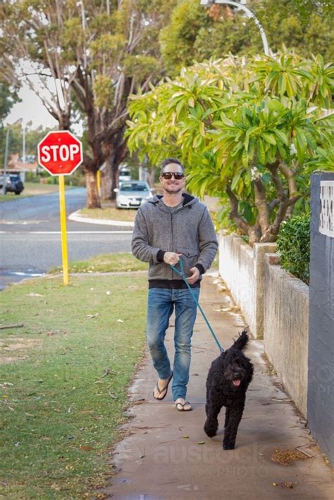 Image of Man walking black dog along suburban street - Austockphoto