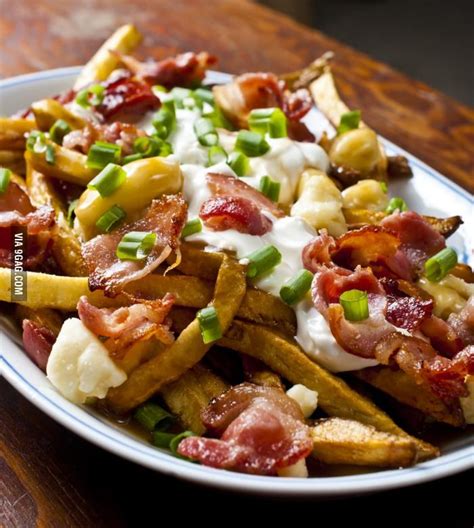 a white plate topped with french fries covered in bacon and ranch dressing on top of a wooden table