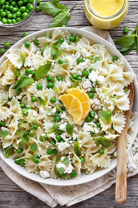 a white bowl filled with pasta and peas next to a glass of orange juice on a wooden table