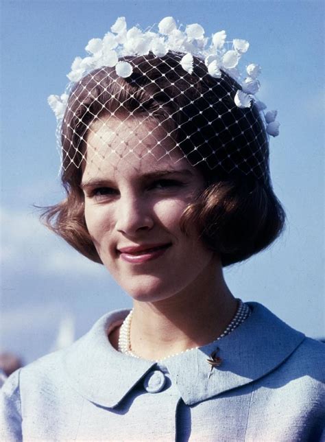 a woman wearing a hat with flowers on it and a veil over her head is ...