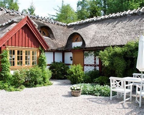 a house with thatched roof and white chairs in front of it, surrounded by greenery