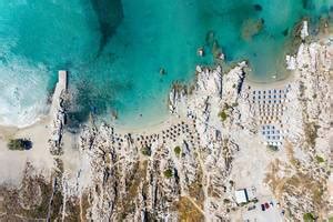 People swimming in the blue sea at Hinitsa Beach, next to restaurant tables under parasols, on a ...