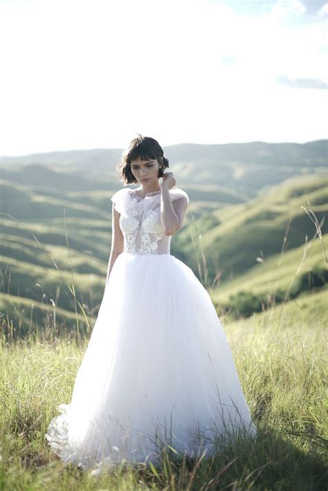 a woman in a white dress standing on top of a lush green field with hills behind her