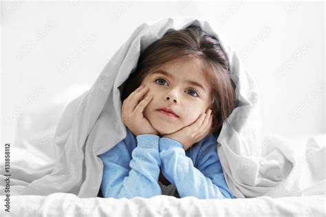 Cute little girl lying on bed under blanket Stock Photo | Adobe Stock