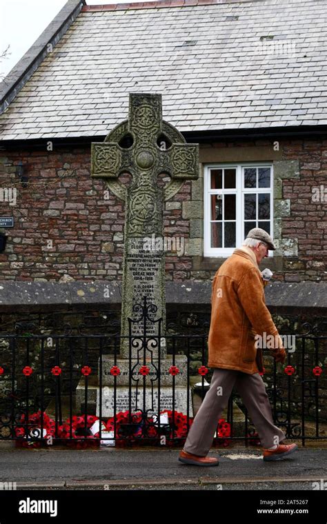 Man walking past poppy wreaths at base of war memorial in Coity village, Mid Glamorgan, Wales ...