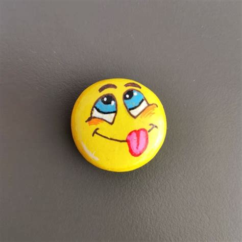 a yellow smiley face with tongue sticking out on a gray surface and grey wall behind it