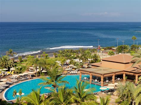 an outdoor swimming pool next to the ocean with palm trees and umbrellas around it