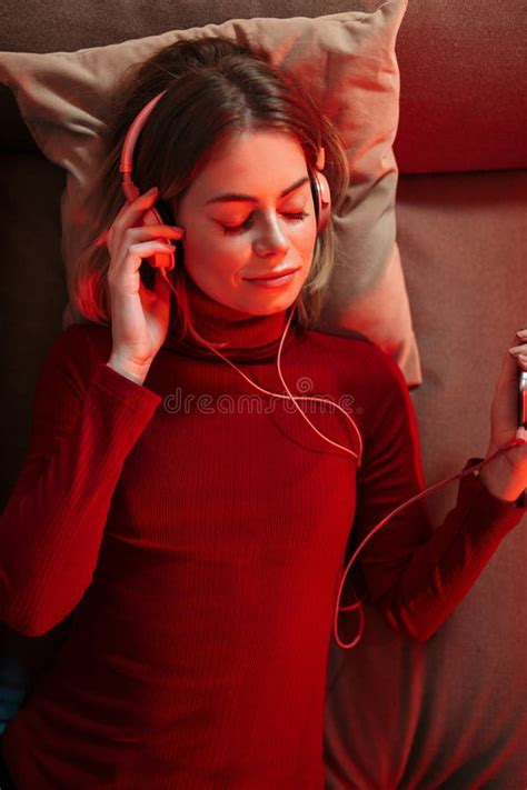 Pensive Lady in Headphones Lying on Sofa with Cellphone in Hand and Listening Music at Home ...