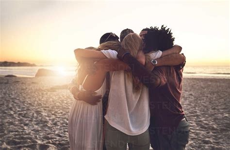 Young friends hugging in a huddle on sunset summer beach stock photo