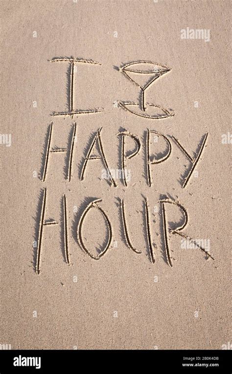 Happy Hour message in the sand featuring a tropical cocktail glass on the beach Stock Photo - Alamy