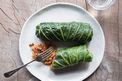 a white plate topped with lettuce covered in sauce next to a fork and glass of water