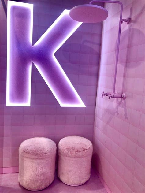 two round stools sit in front of a purple illuminated letter k on the wall