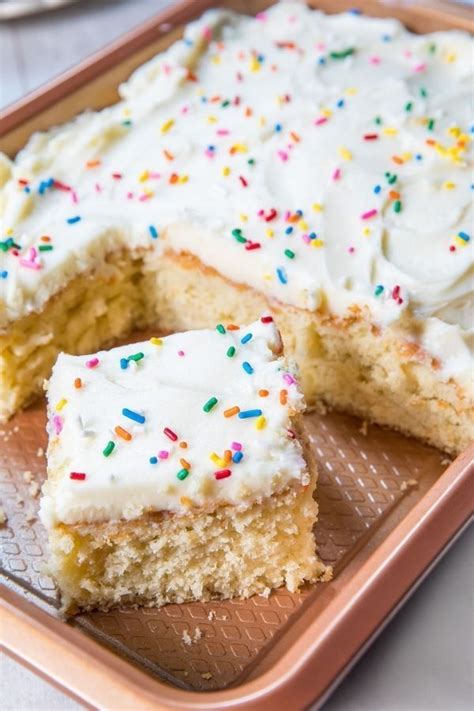 a piece of cake with white frosting and sprinkles sits on a plate