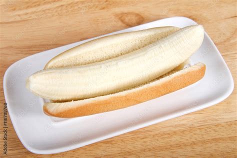 Banana in a hot dog bun served on a white rectangular plate served on a wood table. Top view ...