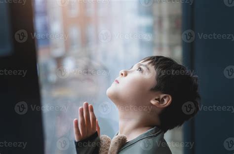 Young kid standing next to window looking up to sky with curious face ...