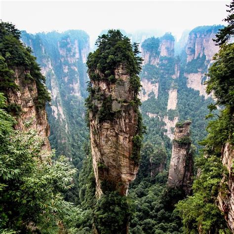 the mountains are surrounded by trees and tall rock formations in the foggy forest area