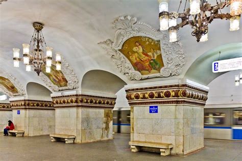 a man sitting on a bench in the middle of a train station with chandeliers hanging from the ceiling