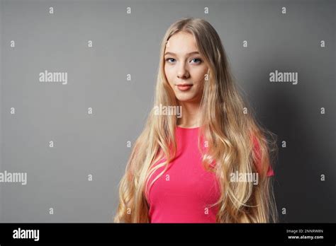 teenage woman with very long blond hair and contented smile against gray background with copy ...