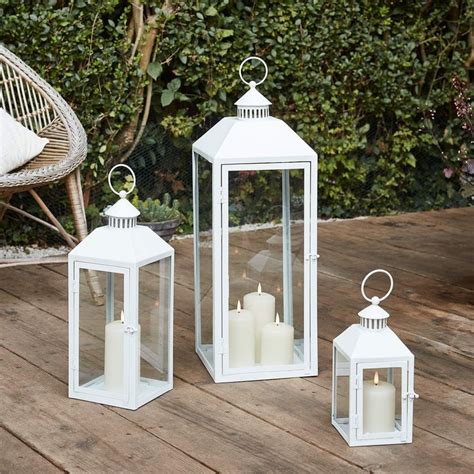 three white lanterns sitting on top of a wooden table