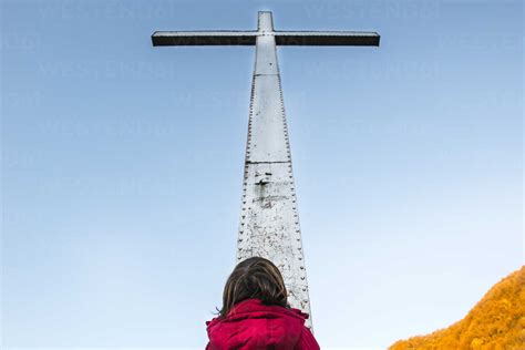 Rear view of boy looking up at towering cross and blue sky stock photo