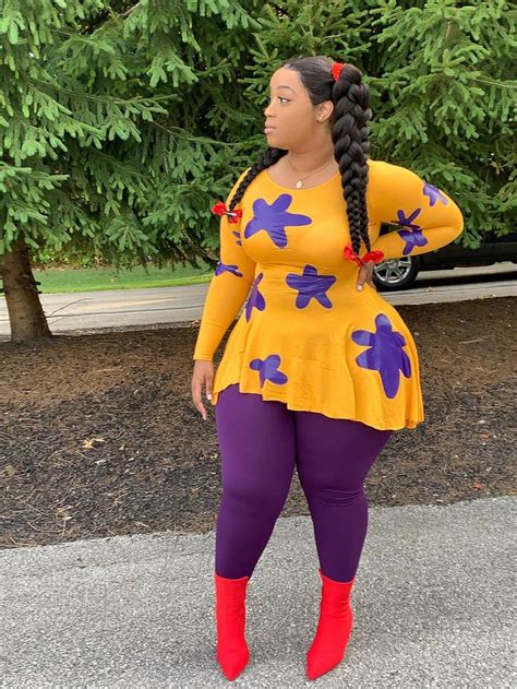 a woman wearing purple and yellow is standing in front of some trees with her hands on her hips