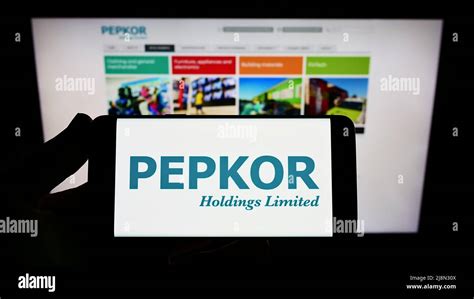 Person holding smartphone with logo of South African company Pepkor Holdings Limited on screen ...