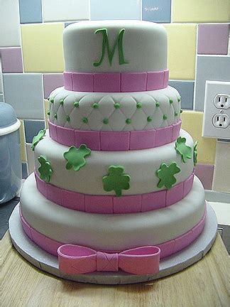 a three tiered cake with pink ribbon and shamrocks on the top, sitting on a counter