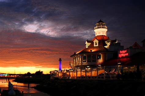 the lighthouse is lit up at night by the water's edge with colorful clouds