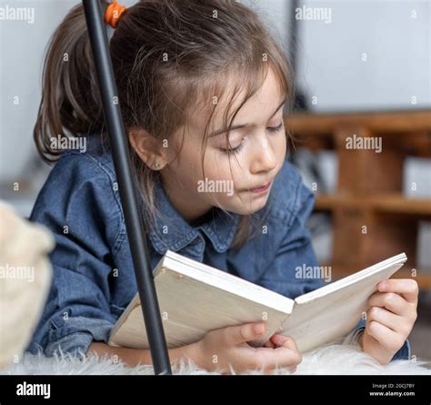 Portrait of a little girl reading a book lying on the floor in the room ...