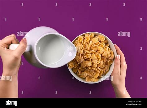 Food and people concept - hands of woman eating cereals corn flakes for breakfast and pouring ...