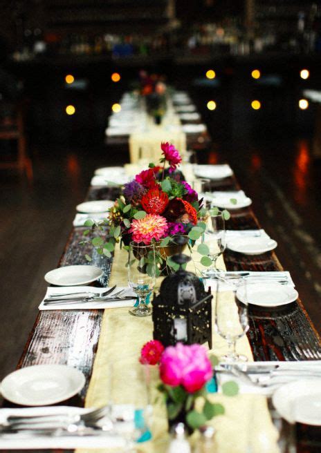 the long table is set with white plates and flowers in vases on each side