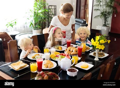 Healthy family breakfast at home. Mother and kids eating tropical fruit, toast bread, cheese and ...