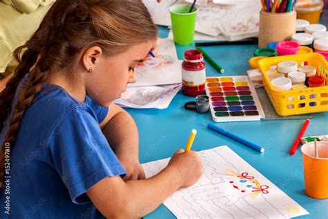 Small student girl close-up painting in art school class. Child drawing by paints on table ...