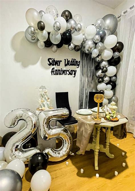 a table with silver and black balloons in the shape of numbers on it, next to a balloon arch ...