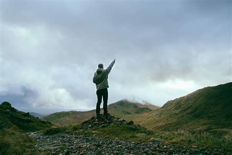 HD wallpaper: man standing on rocks near mountains pointing sky during daytime, man raising his ...