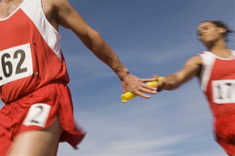 Male athletes passing baton in relay race - The Travel Vertical