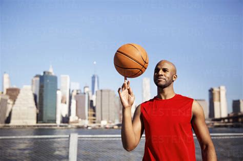 Smiling man spinning basketball on finger against city skyline stock photo