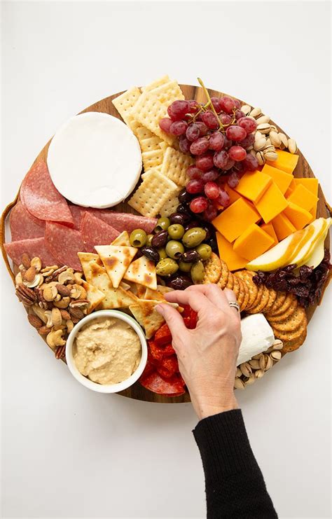 a platter with cheese, crackers, grapes, nuts and meats on it