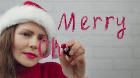 Merry Christmas. Santa Girl Writes Lipstick on Glass Words Merry Christmas. Beautiful Girl in ...