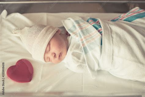 Cute newborn baby boy sleeping in hospital bed with heart next to him. Stock Photo | Adobe Stock