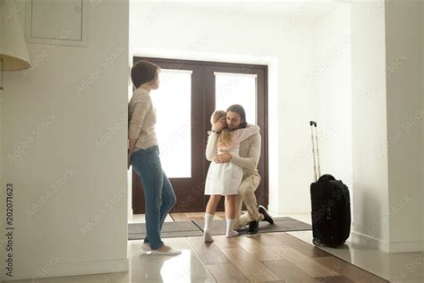 Little kid girl embracing dad leaving family moving out with travel case, sad daughter hugging ...