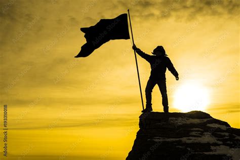 silhouette of man on top of mountain with victory flag, background sky with rays of sunset ...