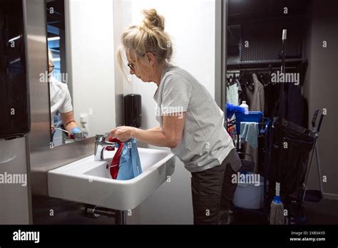 Side view of mature female janitor cleaning sink faucet in bathroom Stock Photo - Alamy