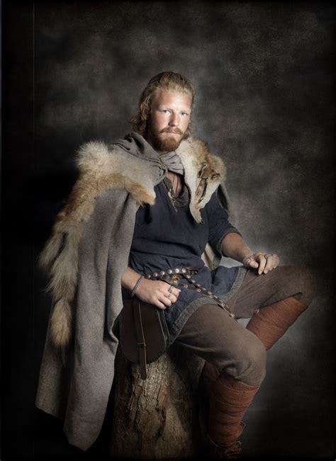 a man with a beard sitting on top of a tree stump wearing a fur coat