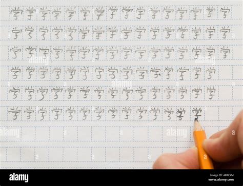 Foreign student learning to write Chinese characters by repetition with pencil and squared paper ...